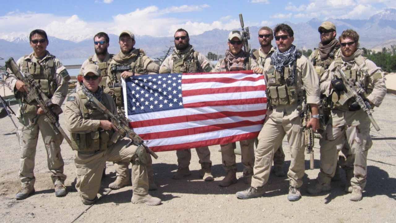 Service members in combat uniforms holding an American flag