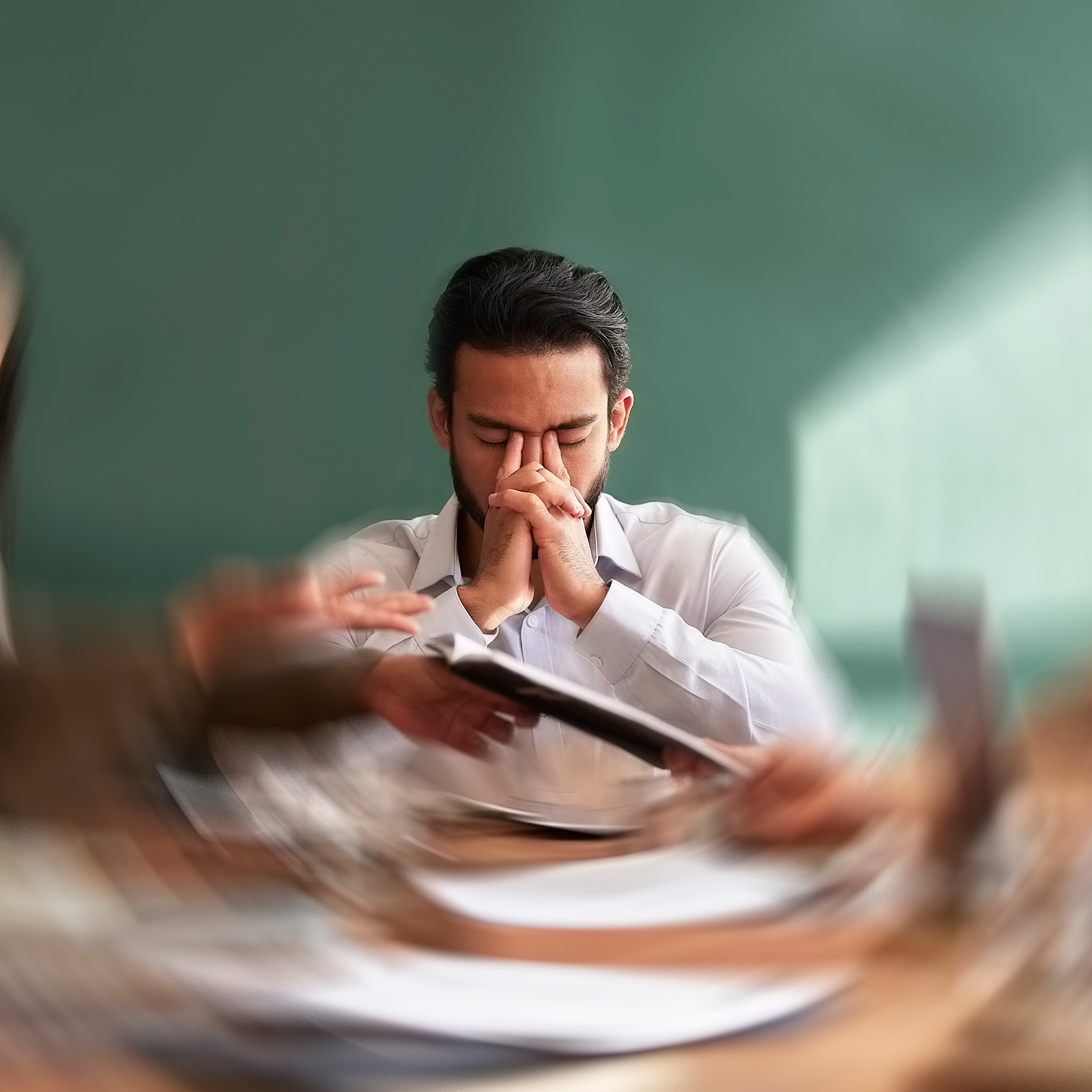 A man with his eyes close in a meeting while everything blurs around him.