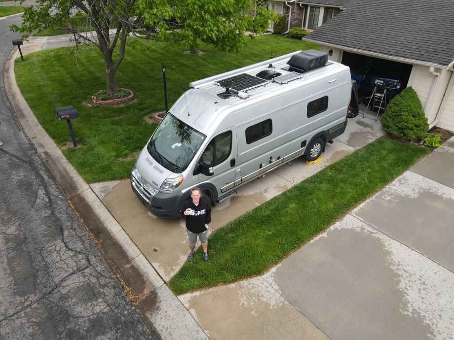 Angela stands in front of her RV home, parked in a driveway, pictured from above by drone.