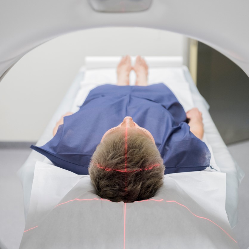 A photo of a person undergoing a CT scan in hospital, lasers forming a faint red cross over the top of their head