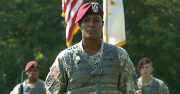 Tonya Oxendine, in uniform, at attention in front of the American and Army 18th Airborne flags