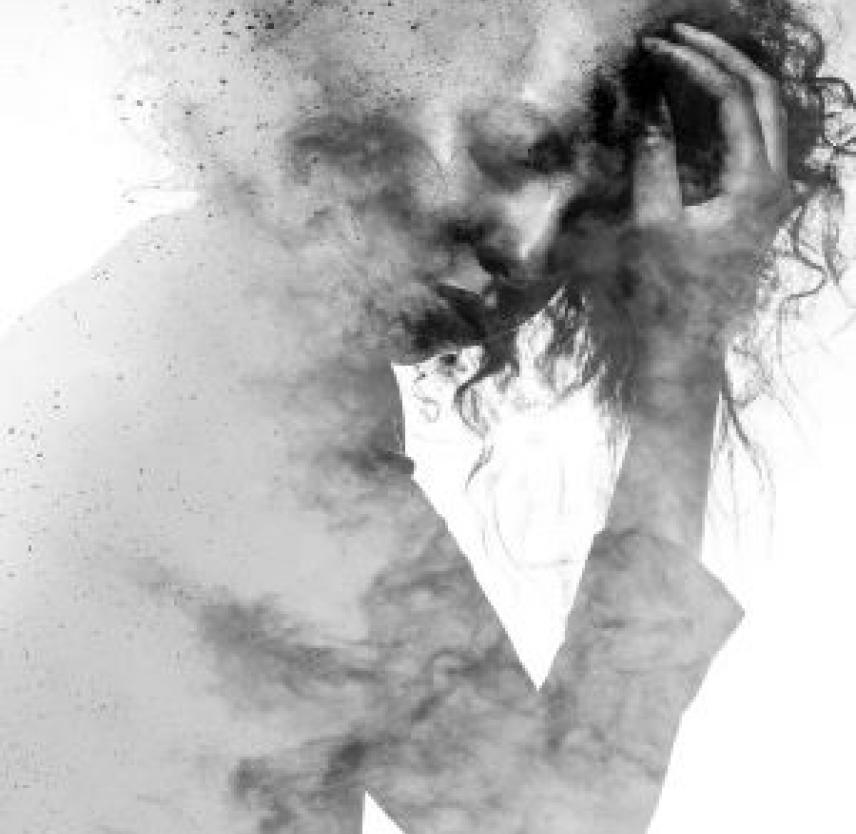Neurofatigue Greyscale image - A woman in a suit cradles her head, with a pained look on her face, obscured by pa