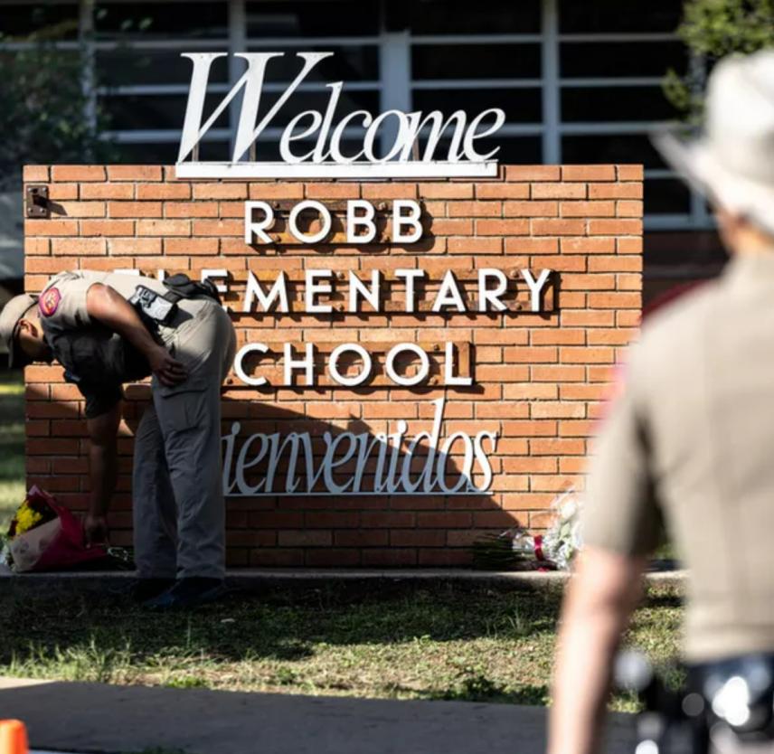 A Texas police officer lays flowers at the Robb Elementary School sign after a mass shooting.