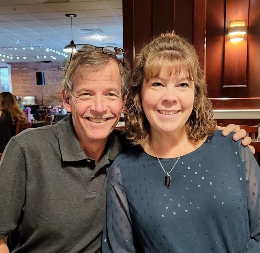 David Grant and his wife smiling in a restaurant with brick and wood paneled walls