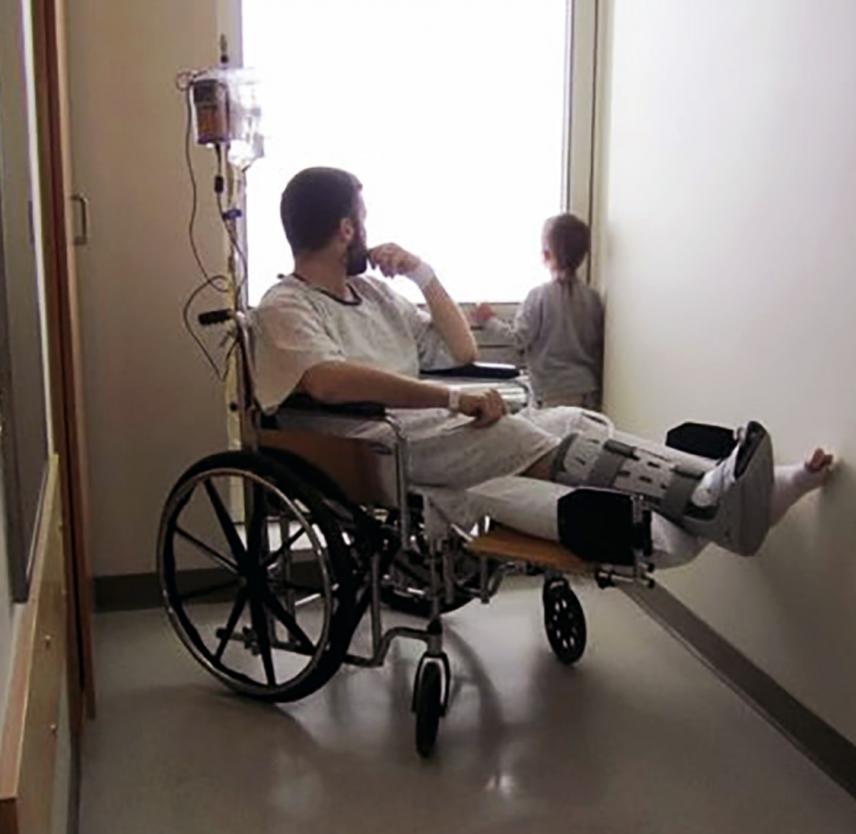 Navy Ensign Timothy Bleigh in a wheelchair looking out a hospital window with his son