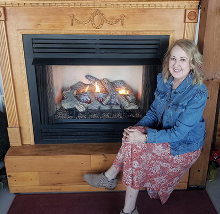 Norma sitting by a blonde wooden fireplace