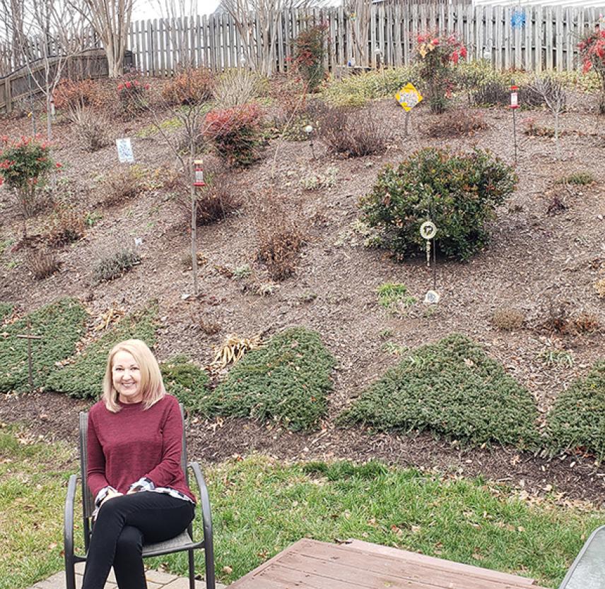 Norma smiling in front of her large retaining wall garden