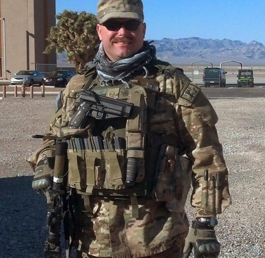 MSgt Ware at a training exercise MSgt Ware in uniform and loaded tactical vest, armed, in front of a distant mountain range