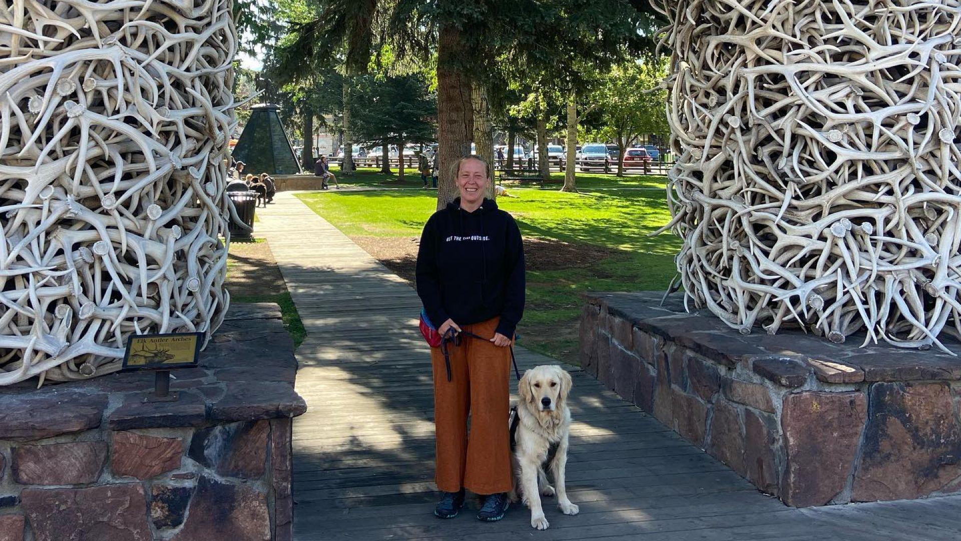 Angela and her service dog Raider stand under Jackson Hole's Elk Antler Arch at Yellowstone National