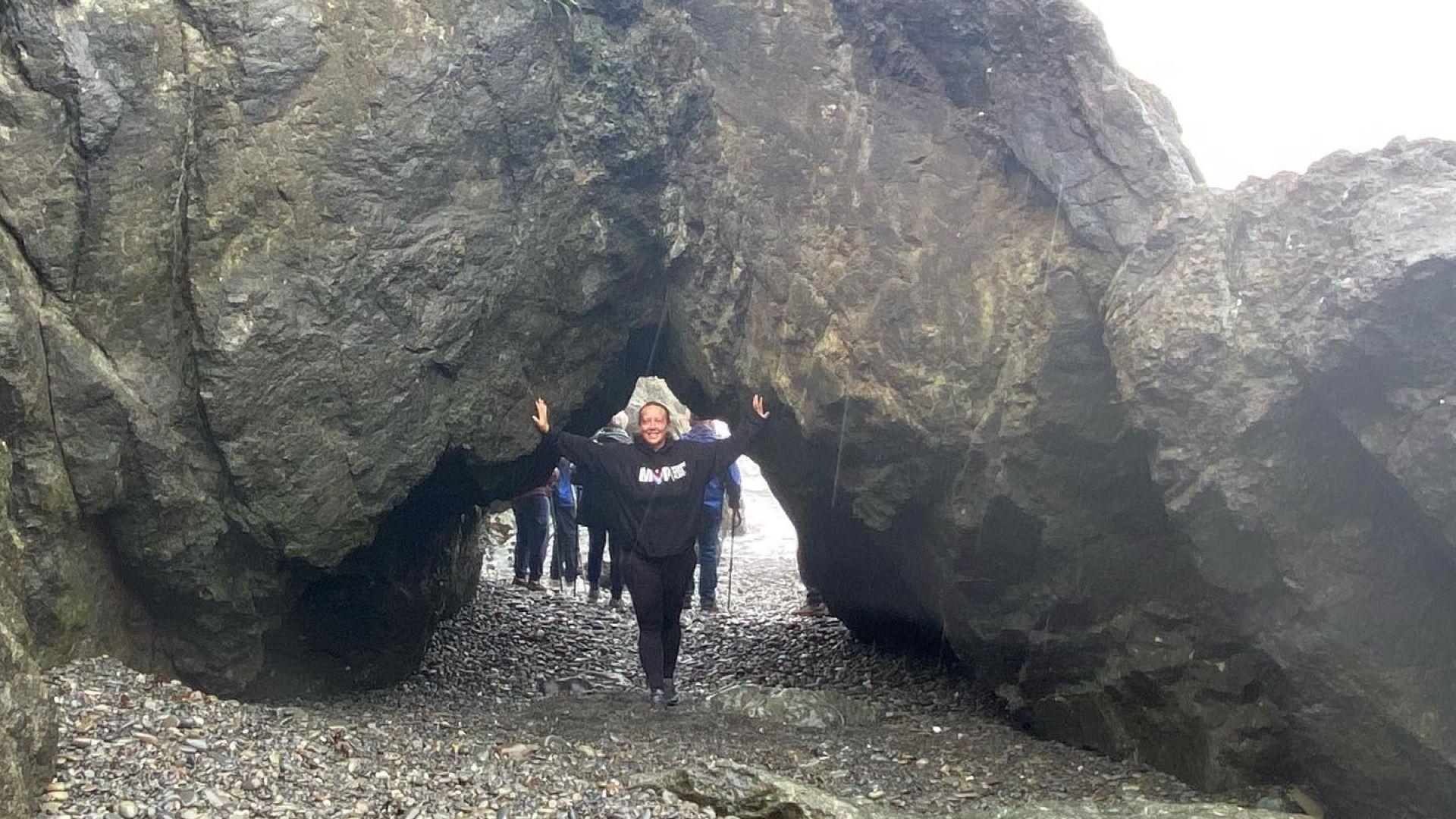 Angela, standing, presses her arms against a tall stone cove at the beach
