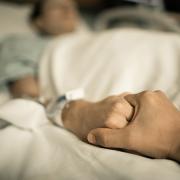 Person holding a loved one's hand in hospital bed