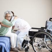 A nurse helps an elderly woman into a wheelchair from a bed