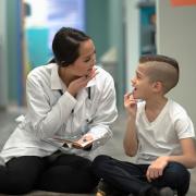 Woman in white lab coat illustrating speech sounds to a boy.