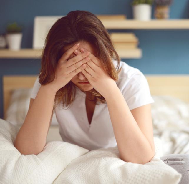 Stress Reactions Woman, seated on a bed, holding her head in her hands, stressed