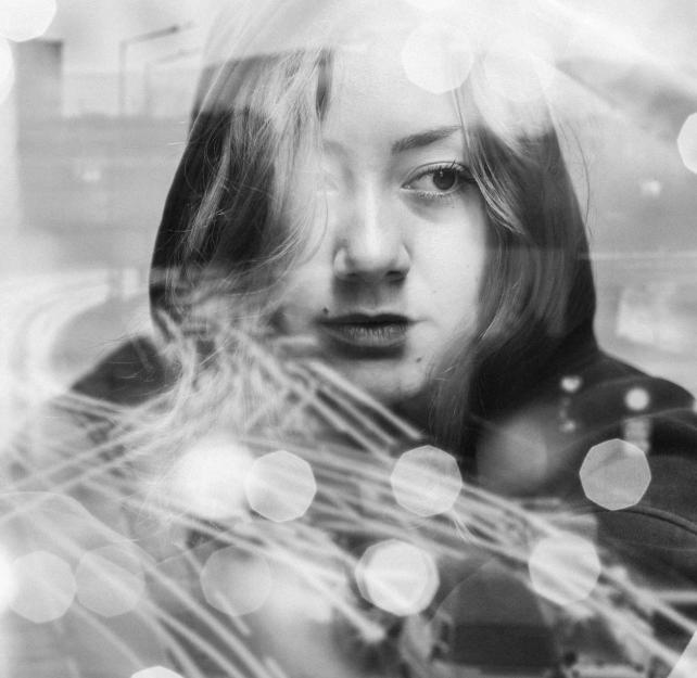 Unhappy young woman sits outside with a confusing array of reflections and lights over her