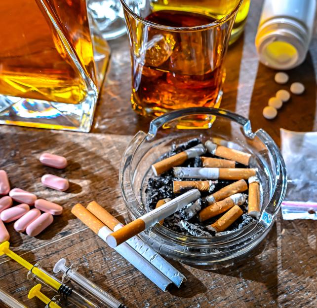 A table covered in cigarettes, syringes, pills, and bottles.
