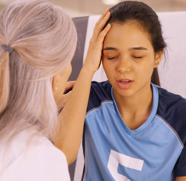 Young soccer player winces as she touches her head, consoled by an older woman facing her