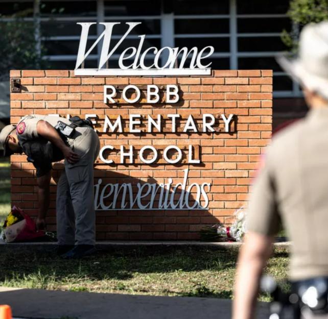 A Texas police officer lays flowers at the Robb Elementary School sign after a mass shooting.
