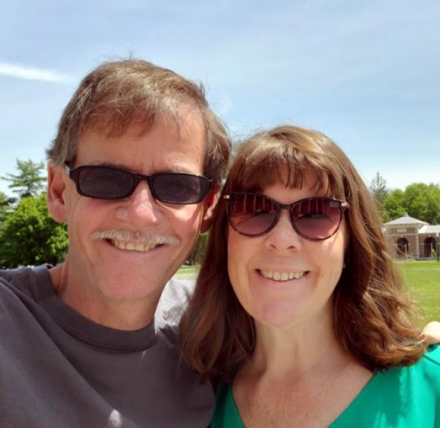 David Grant and his wife smiling in front of a brick building with columns