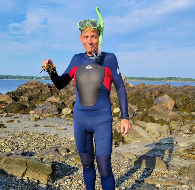 David Grant in a wet suit and snorkel holding a crab at the beach