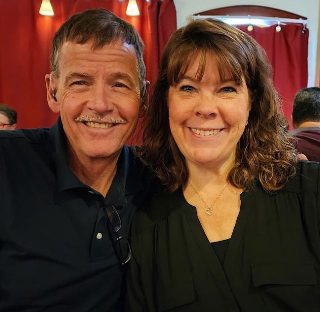 David and his wife smiling in a restaurant, in front of red drapes
