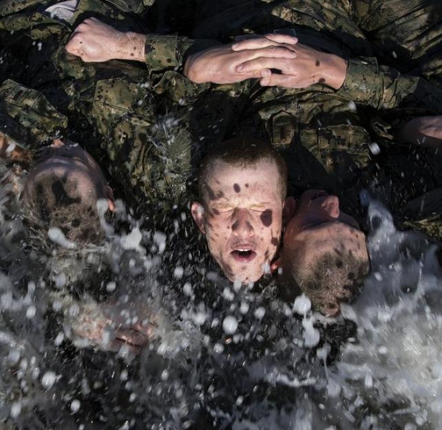 U.S. Navy SEAL candidates participate in Basic Underwater Demolition/SEAL (BUD/S) training, ocean water splashing the faces of uniformed candidates as they interlink arms