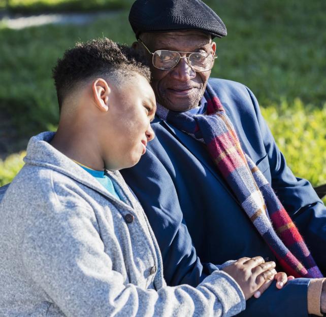 Photo of a young black man resting his head on an elderly black man's shoulder