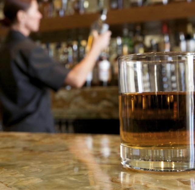 Glass of alcohol on a bar with the bartender and liquor bottles in the background