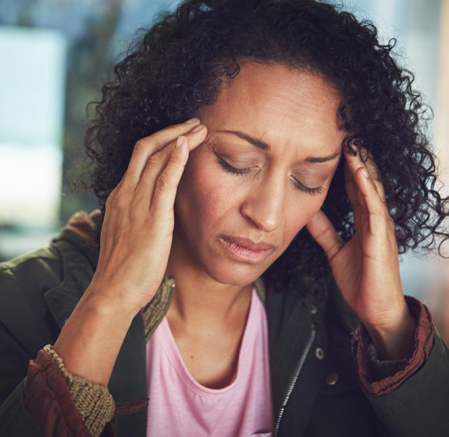 Coping with Caregiver Burnout & Compassion Fatigue Photo of a woman with a pained or tired expression on her face, pressing against her temples with her fingtertips