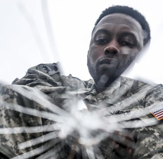 Photo of a uniformed service member reflected in shattered mirror