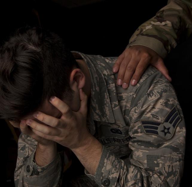 Photo of a uniformed service member with his head in his hands and the outstretched hand of another service member on his shoulder