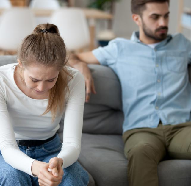 woman with head down and man on couch behind her