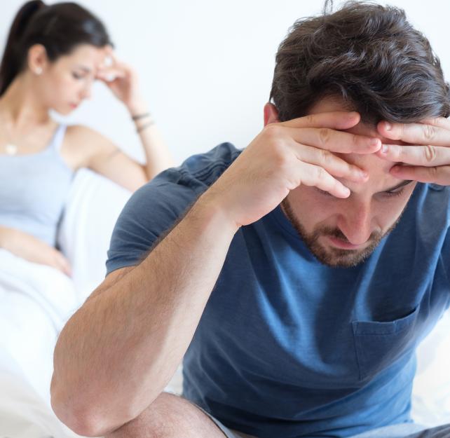 man and woman sitting on bed looking frustrated
