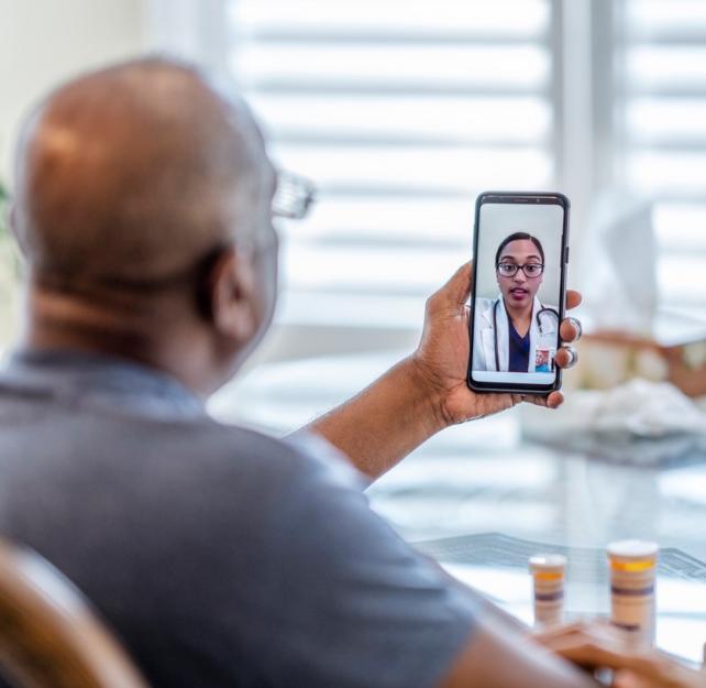 Photo of a man holding his mobile phone on a video call with a doctor on the screen
