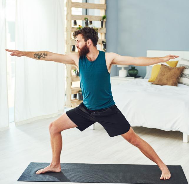 Man doing yoga warrior pose in a sunlit room.