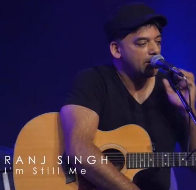 Screenshot from the video of the singer, Ranj Singh, sitting on a stool, speaking into a microphone