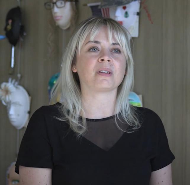Art Therapist Stephanie Clark sitting in front of a wall of masks