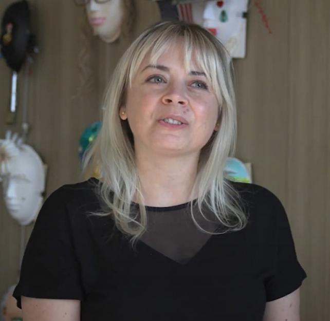 Art Therapist Stephanie Clark sitting in front of a wall of masks