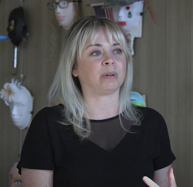 Art Therapist Stephanie Clark sitting in front of a wall of masks
