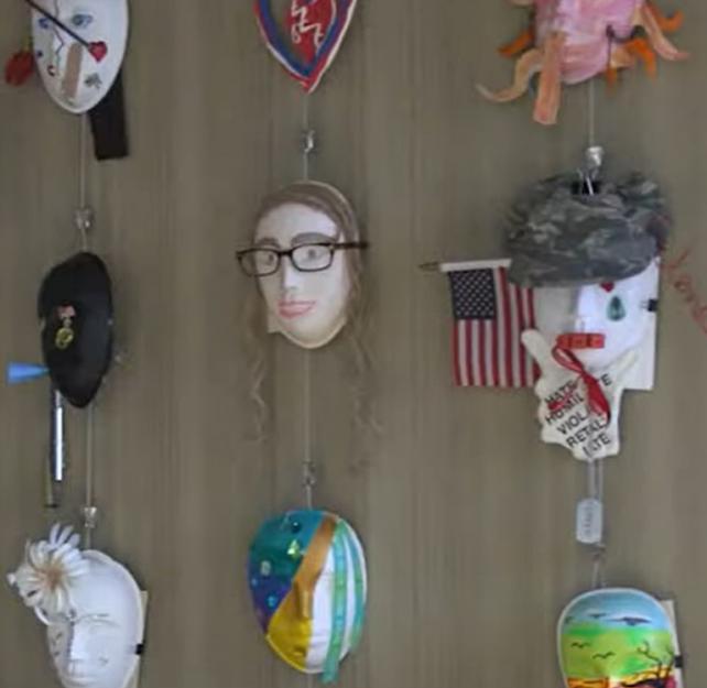 Veteran art therapy masks on display in rows on a light wood wall