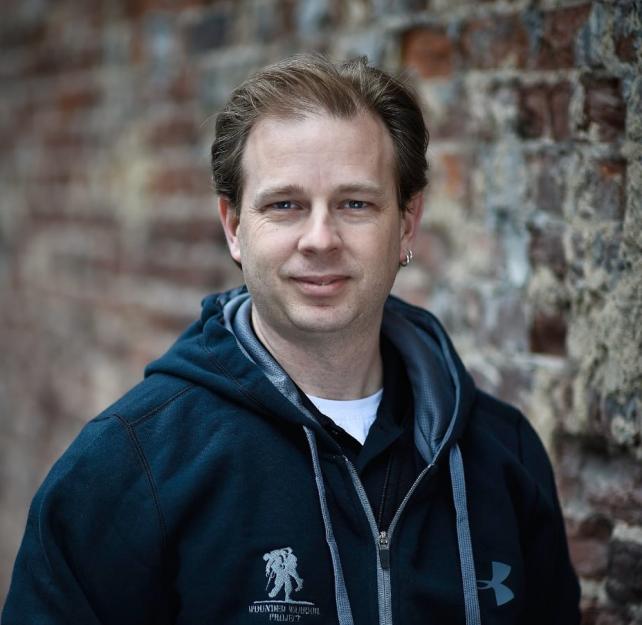 U.S. Army Veteran Bill Jones stands by a brick wall wearing a black Wounded Warrior Project hoodie