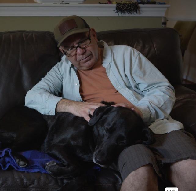 U.S. Army veteran Victor Hurtado petting his service dog Holly on a sofa