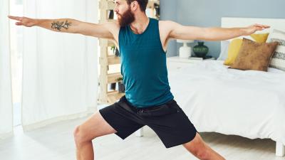 Man doing yoga warrior pose in a sunlit room.
