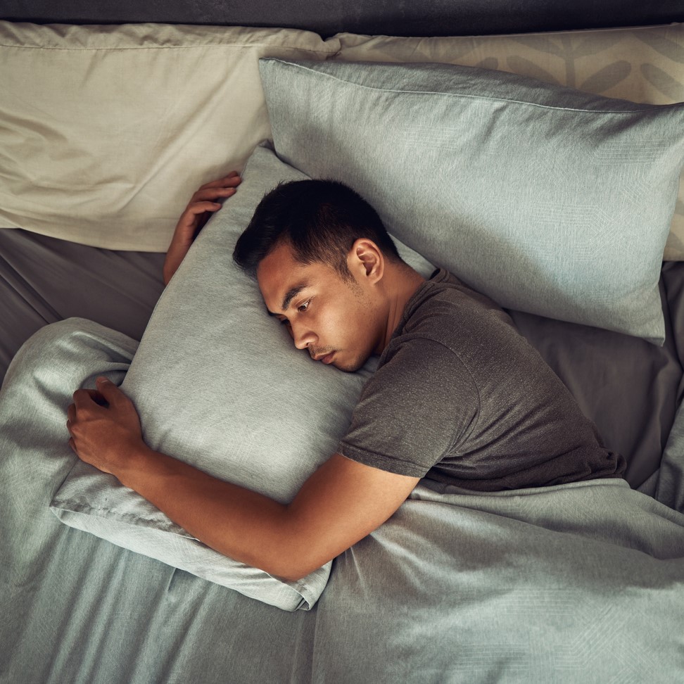 Photo of a young man lying in bed awake and looking unhappy