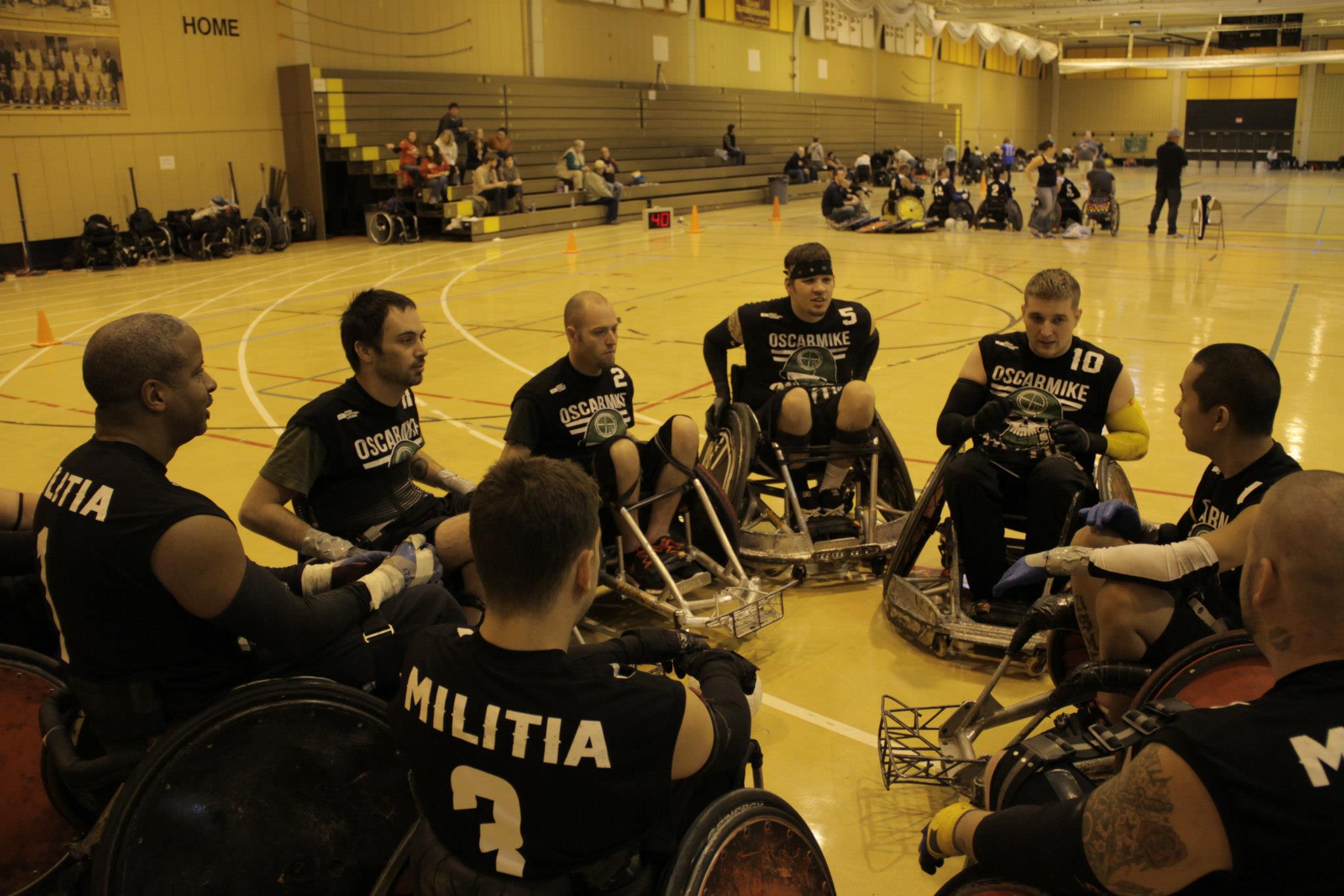 Several OscarMike wheelchair basketball players in a circle huddle on a basketball court